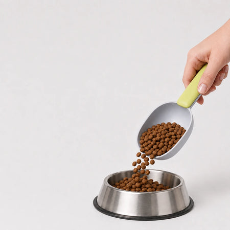 Pet food scooper pouring dry dog food into a stainless steel bowl