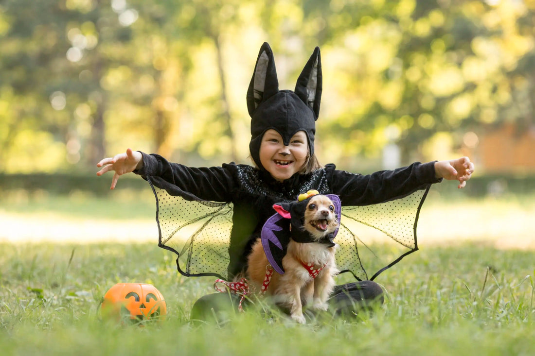 Child dressed as a bat sitting with a small dog in a Halloween costume, perfect for pet and kids Halloween photoshoots.