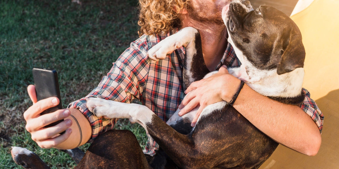 Man taking a selfie with his dog in a garden using a smartphone, showing the close bond between pet and owner.