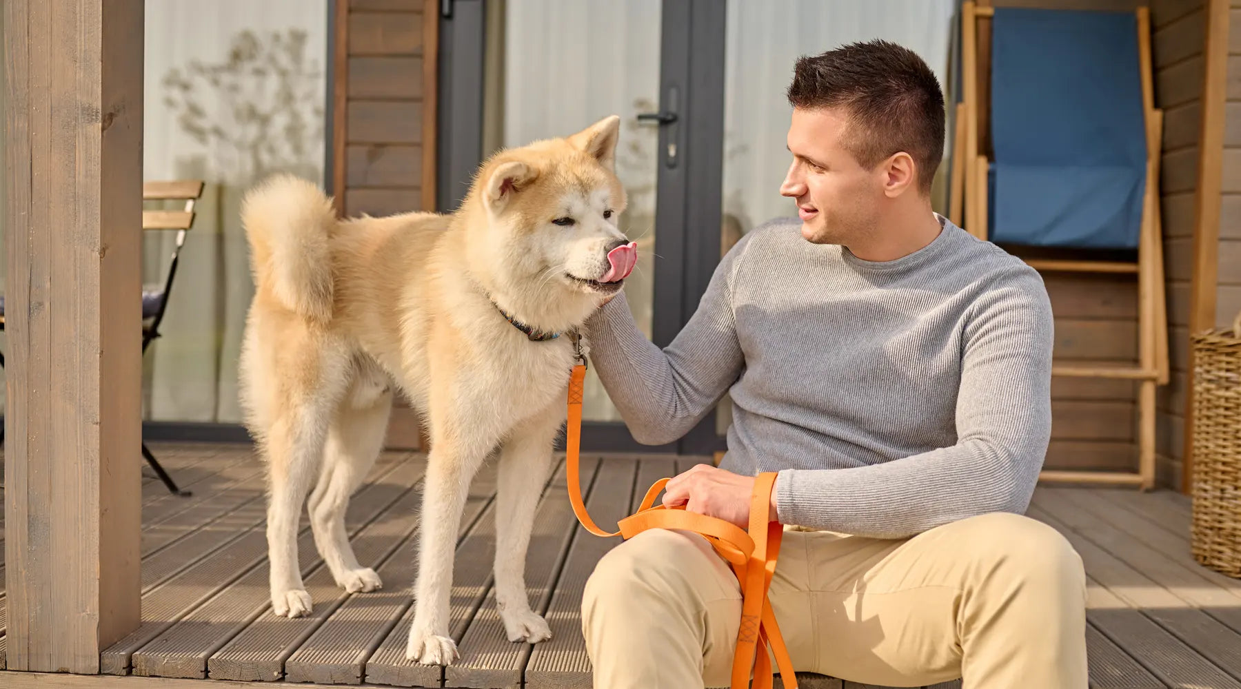 Man sitting on a porch holding a dog on a leash while spending time together at home