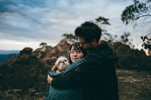 Couple embracing their small dog outdoors, showcasing pet love and companionship in nature.