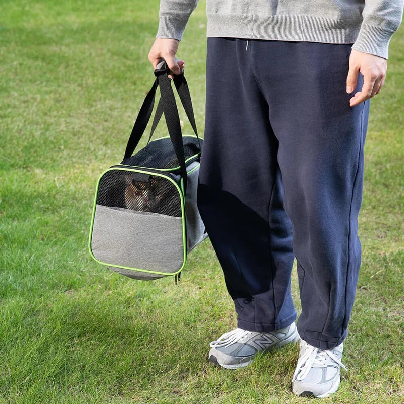 Person carrying a gray and green airline-approved pet carrier bag with a mesh front, perfect for travel with small pets.