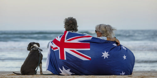 Couple sitting on the beach wrapped in Australian flag with dog - explore budget pet supplies online in Australia