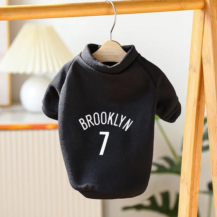 Black brooklyn nets dog sweater on a hanger in a cozy room