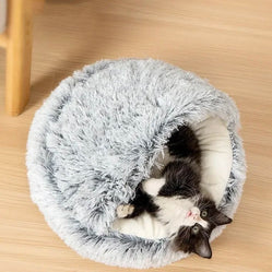 Black and white cat relaxing inside a cozy cave cat bed on a wooden floor