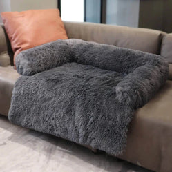 Dark gray dog bed couch shown on a sofa with bolstered sides