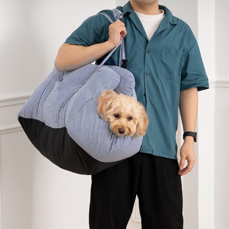 Man carrying a small dog in a portable blue striped dog car seat with seatbelt, ideal for travel and comfort.