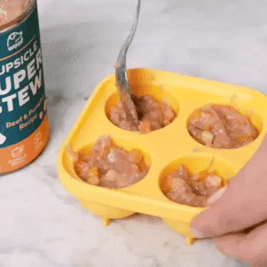 hand filling a mould with dog food and placing it in the freezer to prepare a dog lick ball toy