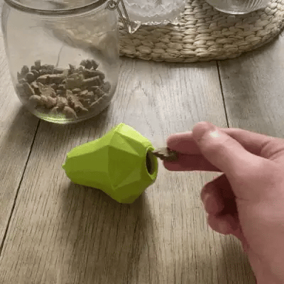 hand placing a treat into a dog toy hide treats opening on a wooden table