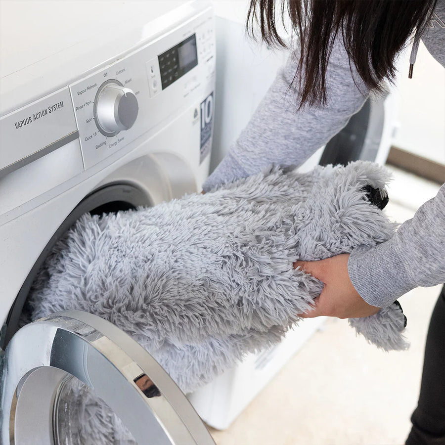 Woman loading a dog bed cover for couch into a front load washing machine in a bathroom