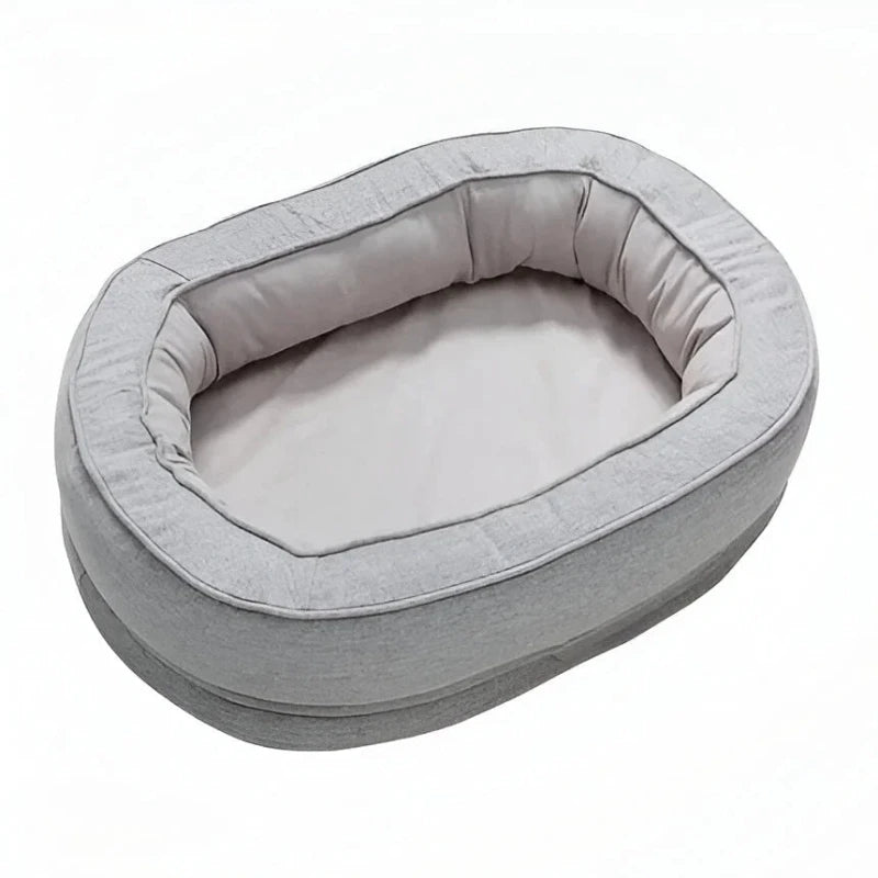 Grey oval dog bed with padded bolster on white background