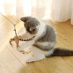 A cat sitting on the floor batting a cat bird teaser toy indoors