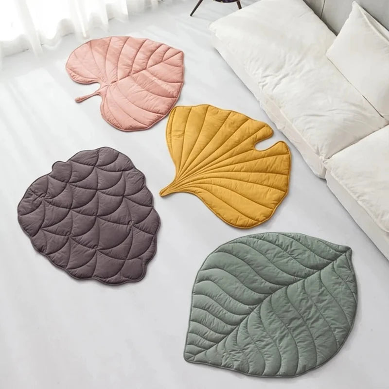 Four colorful leaf-shaped pet mats in pink, yellow, grey, and green displayed in a modern living room setting.