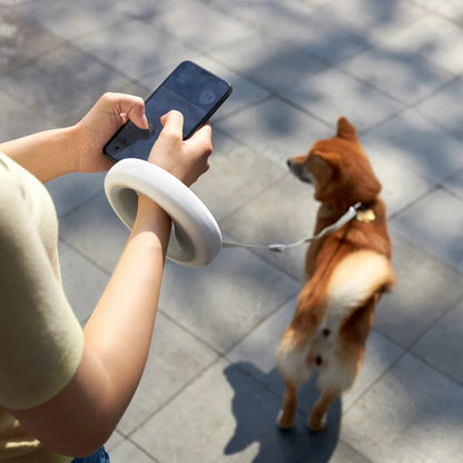 A person using the MOESTAR UFO retractable dog leash while checking their phone, with a dog in the background.