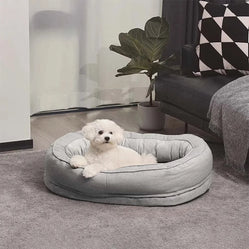 Small oval pet bed in gray with white dog resting in living room