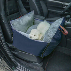 Small white dog resting in a comfy blue travel bag inside the car.