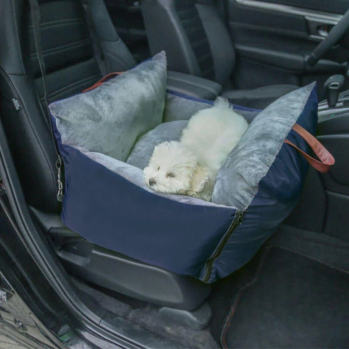 Small white dog resting in a comfy blue travel bag inside the car.