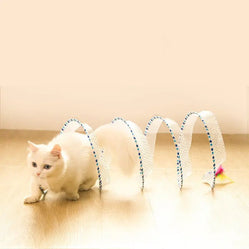A white cat moving through a cat hunting spiral toy on a wooden floor