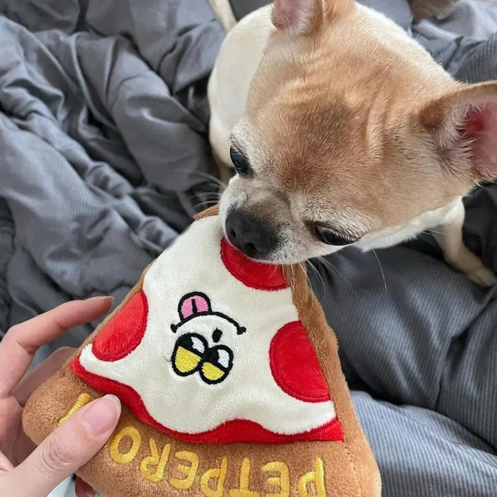 Cheesy pizza dog toy being held and chewed by a small dog on a bed